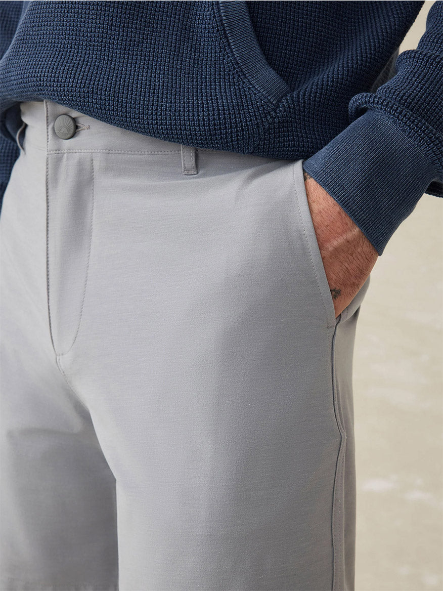 A person wearing Faherty Brand All Day Short in Ice Grey—crafted with water-repellant fabric—and a dark blue textured long-sleeve shirt, one hand in the pocket.
