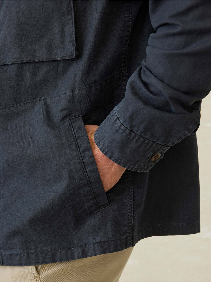 A person wearing the Faherty Brand Commander Shirt Jacket in Washed Charcoal with their right hand in the pocket, paired with beige pants, showcases breathable comfort and rugged durability.