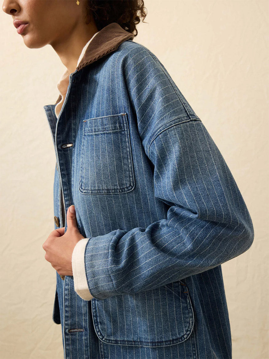A person wearing the Faherty Brand Sunwashed Denim Barn Jacket in Dusk Stripe Wash, featuring a brown corduroy collar, is shown from the side against a plain, light background.