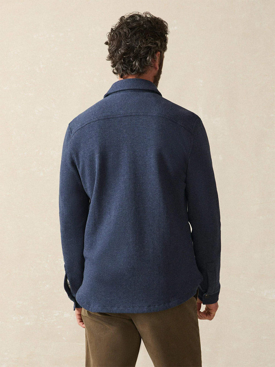 A man with curly hair, seen from behind, wears the Faherty Brand Inlet Knit CPO in Navy Night Melange and brown pants against a plain light background.
