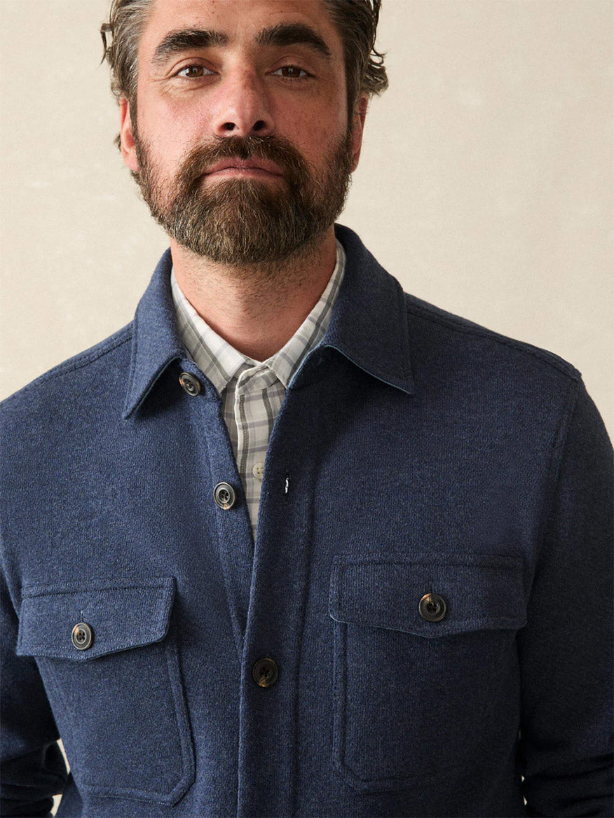 A bearded man faces the camera against a neutral background, wearing a plaid collared shirt layered with the Faherty Brand Inlet Knit CPO in Navy Night Melange.