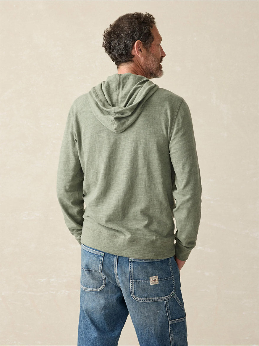 A man stands with his back to the camera, wearing the Faherty Brand Sunwashed Slub Hoodie in Clover Creek, made from American-grown cotton, paired with blue jeans featuring a relaxed fit.