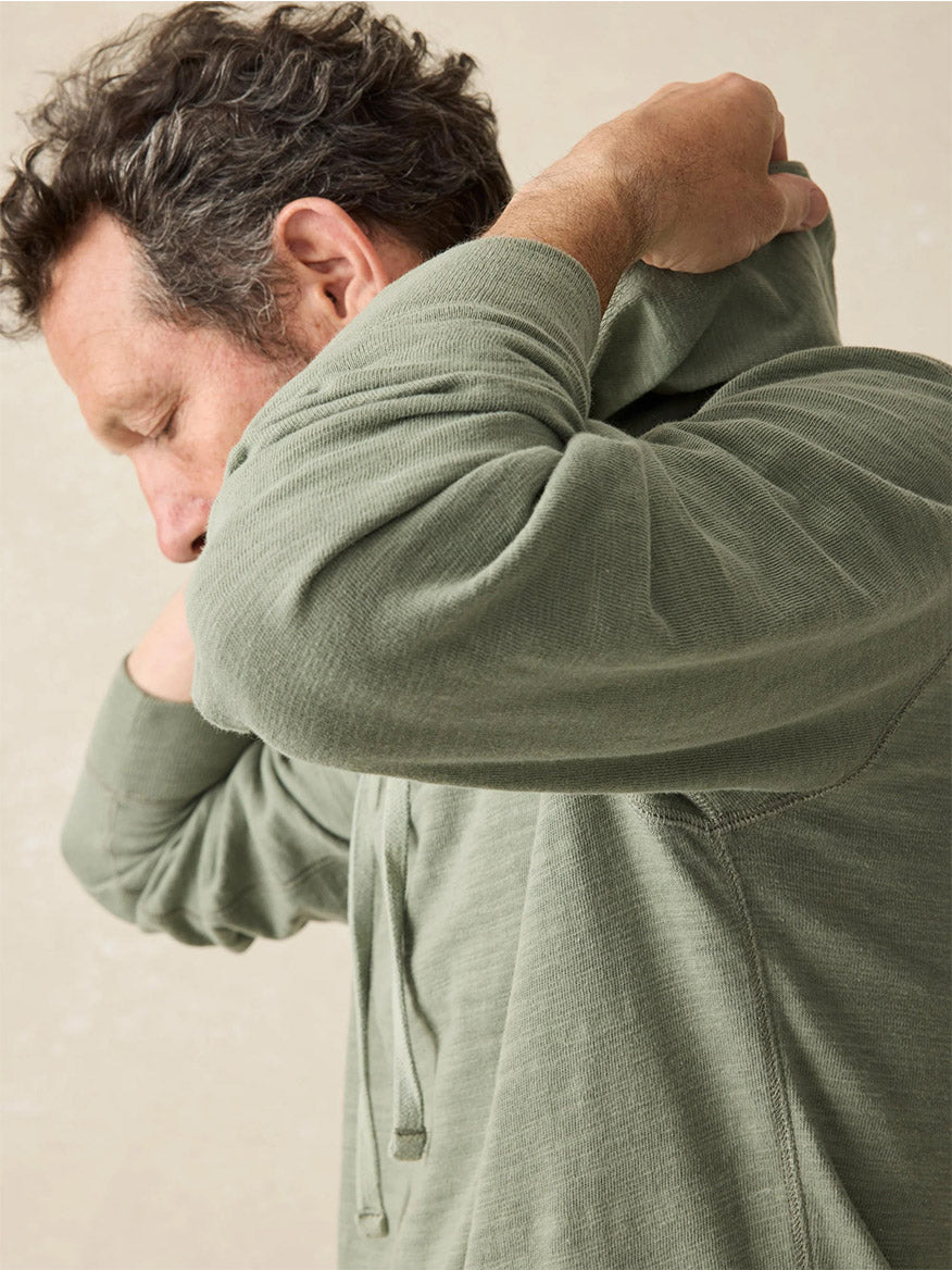 A man wearing the Faherty Brand Sunwashed Slub Hoodie in Clover Creek, made from American-grown cotton, pulls the hood over his head.