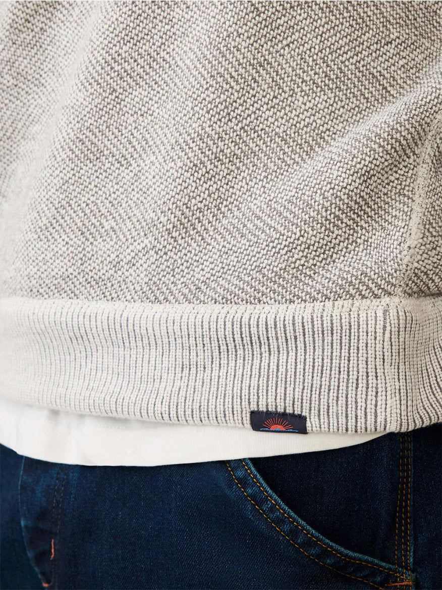Close-up of the Faherty Brand Whitewater Quarter Zip in Grey Shell Loop, a breathable knit sweater with a ribbed hem, worn over a white shirt and dark blue jeans with visible stitching.