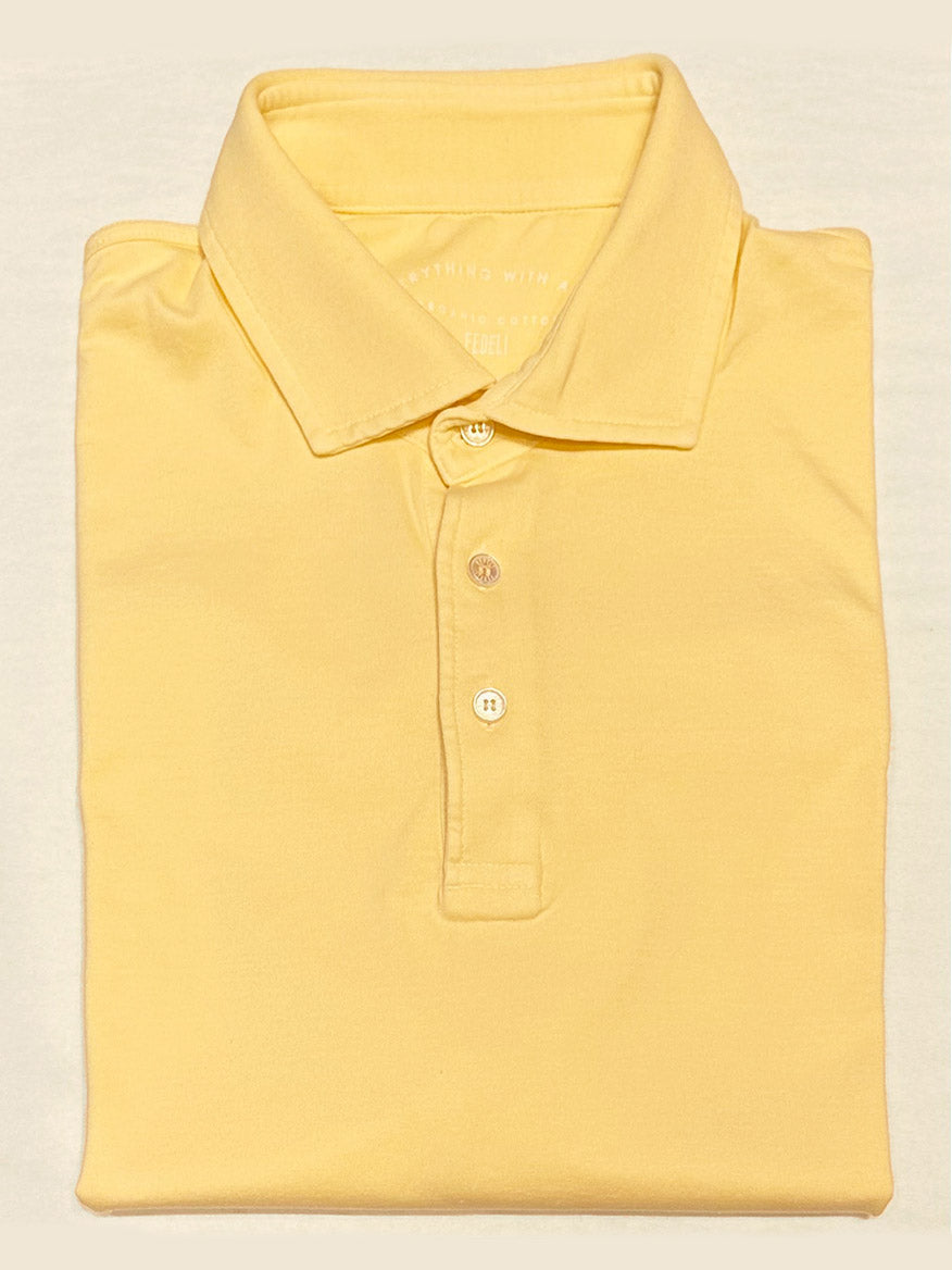 The Fedeli Zero Organic Cotton Short Sleeve Polo in Yellow, made in Italy from premium Giza organic cotton with a collar and three mother of pearl buttons, is neatly folded and displayed on a light surface.