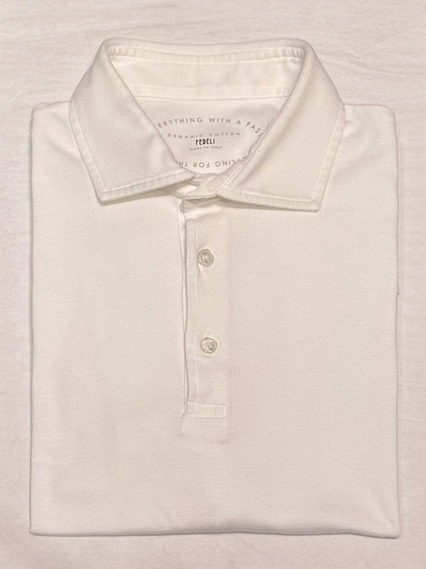 The Fedeli Zero Organic Cotton Short Sleeve Polo in White, crafted in Italy from premium Giza organic cotton and finished with three mother of pearl buttons, is neatly folded and displayed on a flat surface.