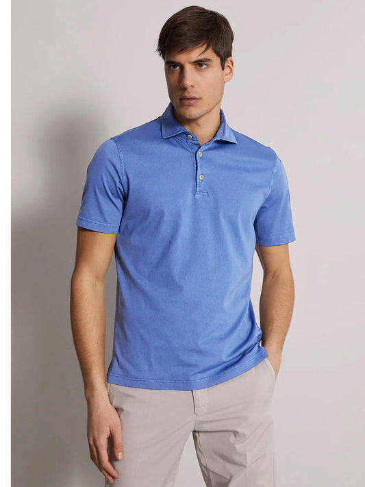 A young man wearing a Fedeli Organic Giza Cotton Polo in Ocean and light beige pants, standing against a neutral background with a slight pose.