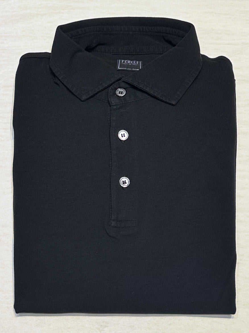 The Fedeli Zero Superlight Pique Short Sleeve Polo in Black, featuring a classic three-button collar and Italian craftsmanship, is neatly folded and viewed from above on a light-colored surface.