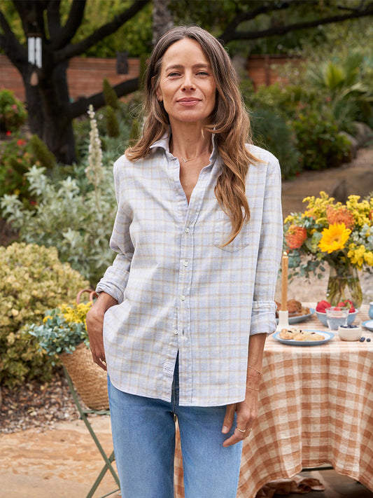 A woman named Eileen standing in a California garden setting wearing a Frank & Eileen Eileen Relaxed Button-Up Flannel Shirt in Camel & Cream with Grey Plaid and jeans with a table set in the background.