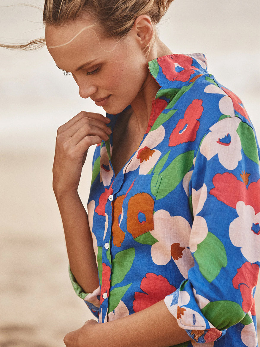 Wearing the Frank & Eileen Mary Classic Shirtdress in Bright Blue Floral, a person stands outdoors looking down gently—a true wardrobe must-have.