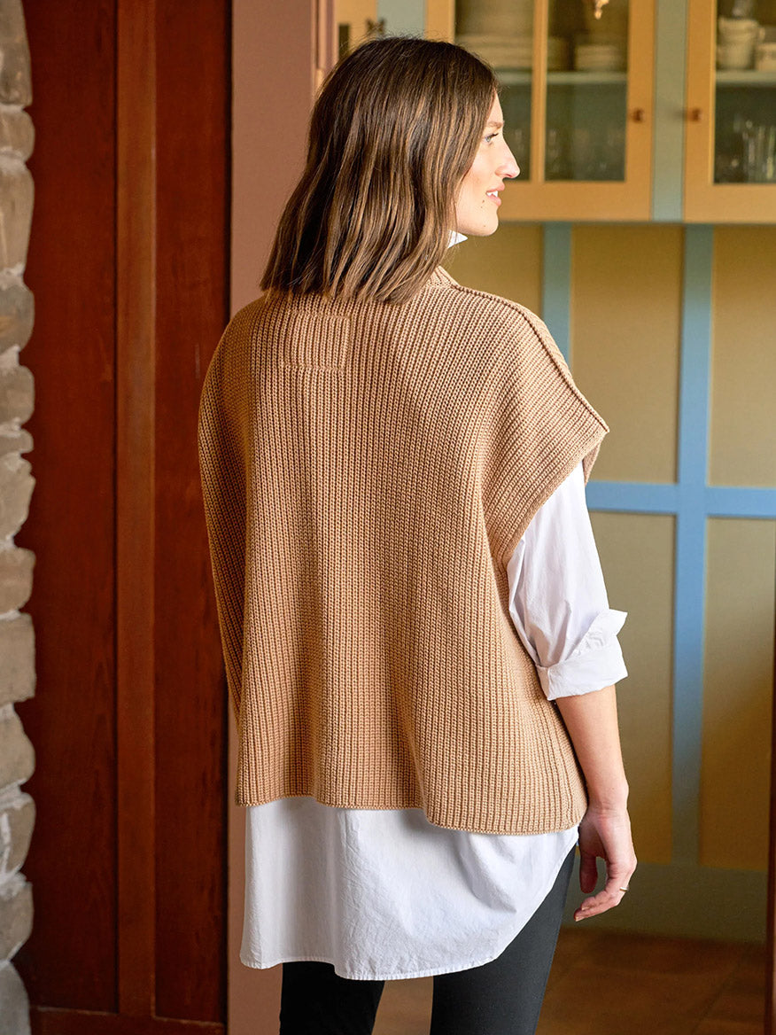A woman stands indoors facing away, wearing a white button-down shirt under the Frank & Eileen Montecito Italian Sweater Vest in Camel.