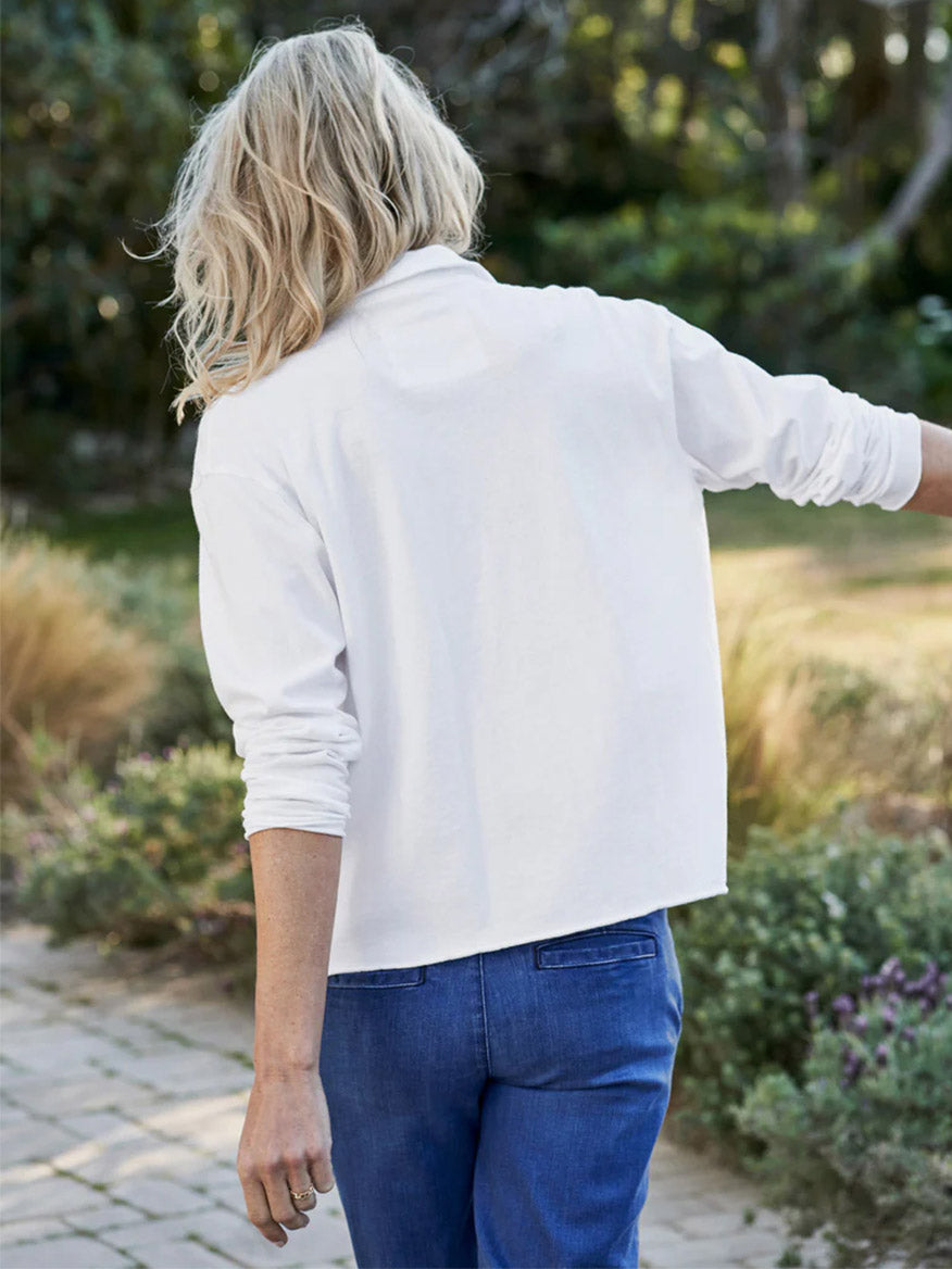 A woman from behind wearing a white Frank & Eileen Patrick Popover Henley in White Heritage Jersey and blue jeans in a garden setting.