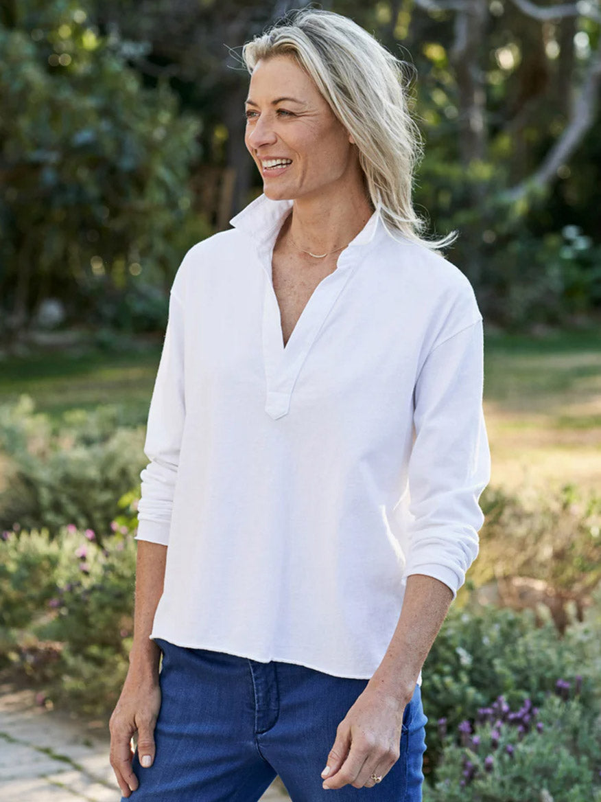 A smiling woman wearing a Frank & Eileen Patrick Popover Henley in White Heritage Jersey and blue jeans standing outdoors.