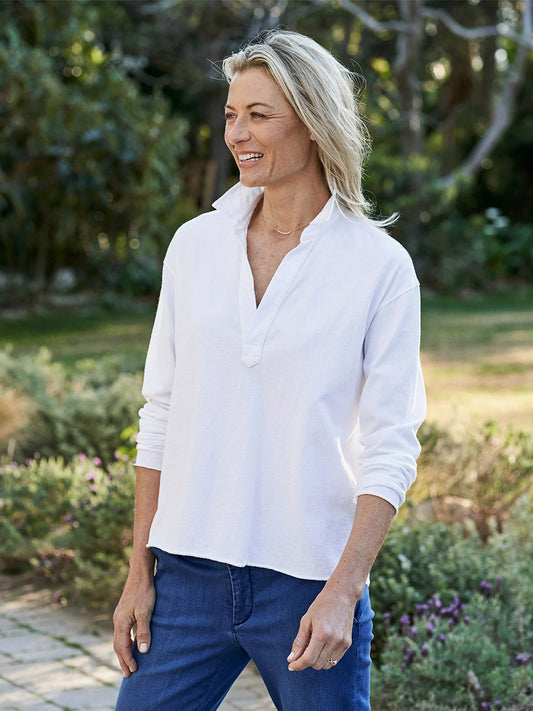 A smiling woman in a Frank & Eileen Patrick Popover Henley in Vintage White Heritage Jersey and blue jeans standing outdoors.