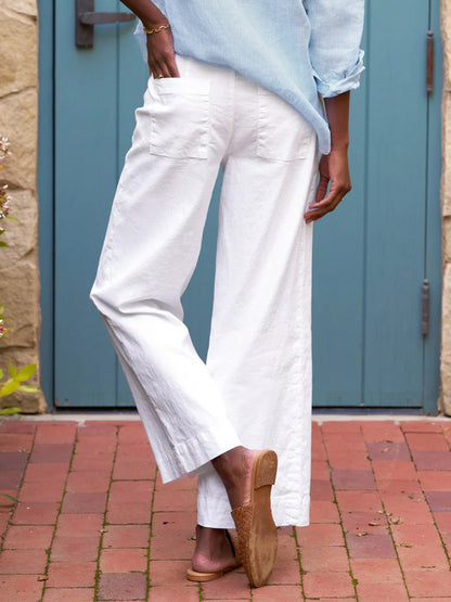 A person standing in an alley wearing Frank & Eileen Wexford Wide-Leg Linen Pants in White and beige loafers, with a glimpse of a blue shirt.