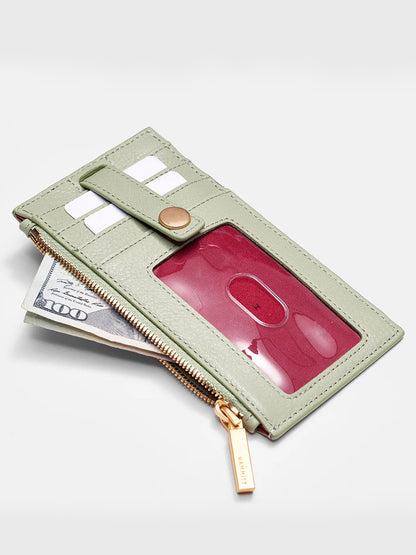 A Hammitt Los Angeles 210 West Wallet in Cypress Sage with a zipper, partially open to reveal a $100 bill, credit cards, and an ID in the clear pocket.