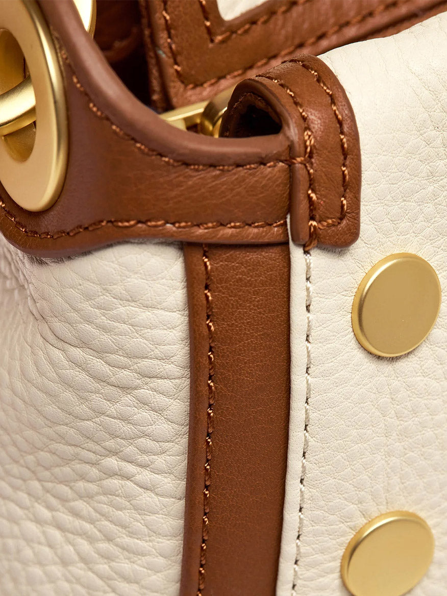 Close-up of the Hammitt Los Angeles Bryant Medium Crossbody Bag in Courtyard Cream, featuring white pebbled leather, brown trim, gold rivets, and a gold metal ring detail.