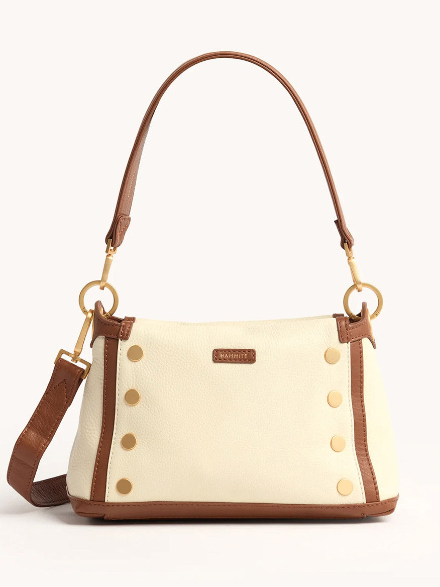 The Hammitt Los Angeles Bryant Medium Crossbody Bag in Courtyard Cream is a cream pebbled leather shoulder bag with brown trim, gold hardware, a detachable strap, and decorative gold studs on the front.