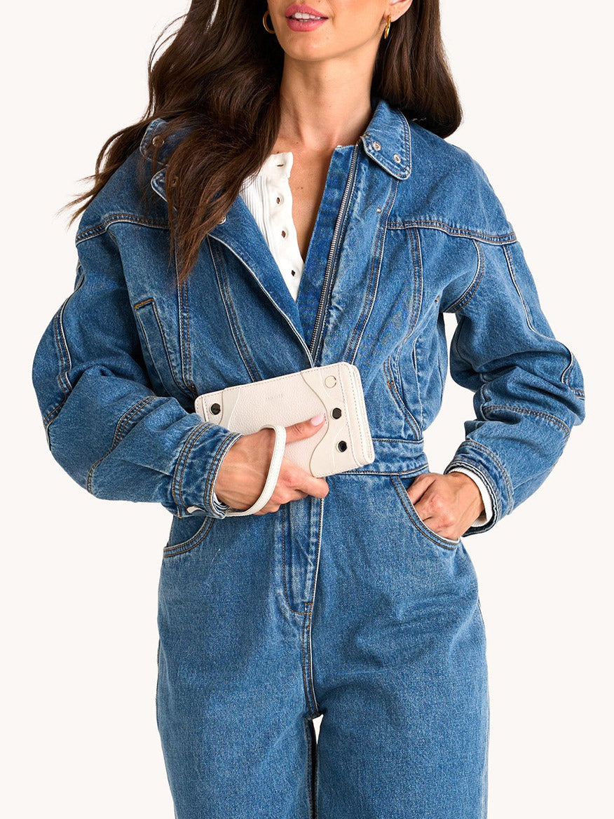 Woman wearing a blue denim jacket and jeans, holding the Hammitt Los Angeles Bryant Wallet in Western Rein/Silver, crafted from pebble leather with a sleek hand strap and detachable wristlet for versatile style.