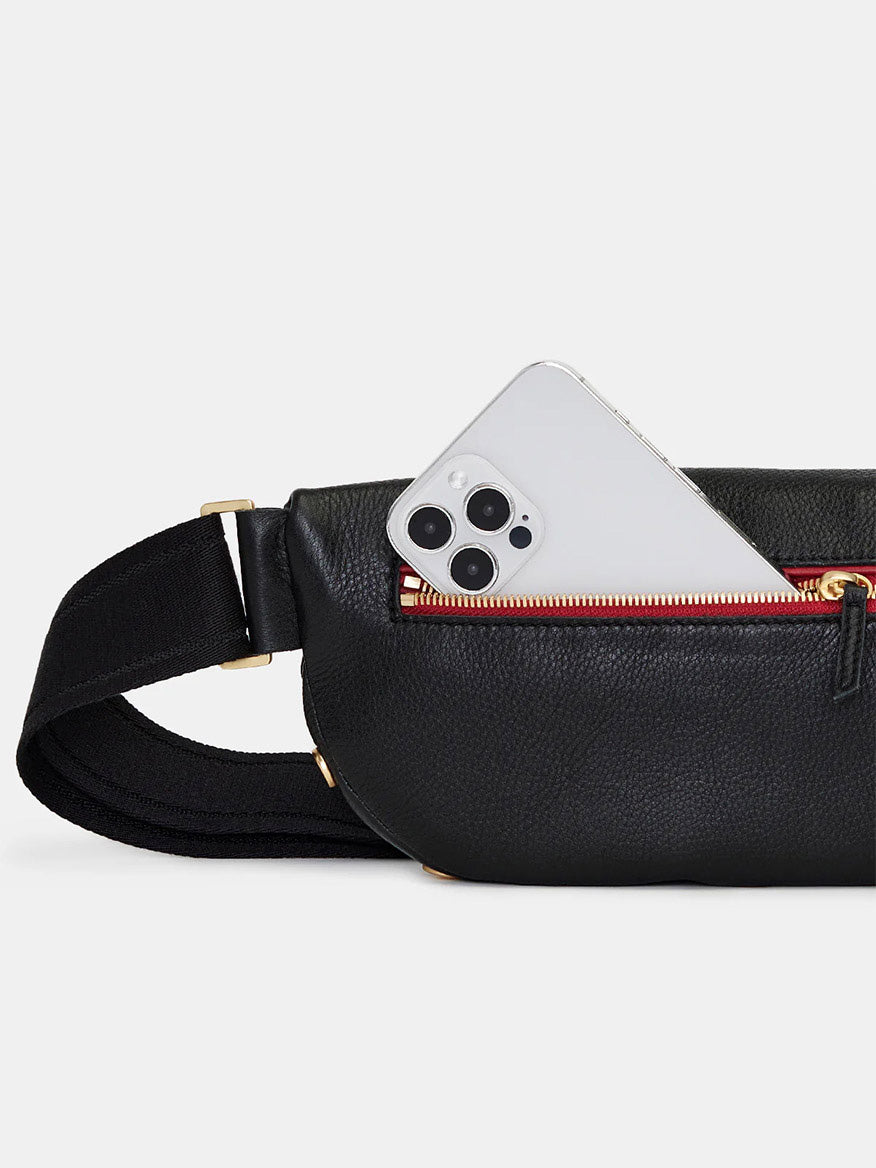 A Hammitt Los Angeles Charles Crossbody Medium in Black/Brushed Gold/Red Zip is partially open, revealing a smartphone inside.