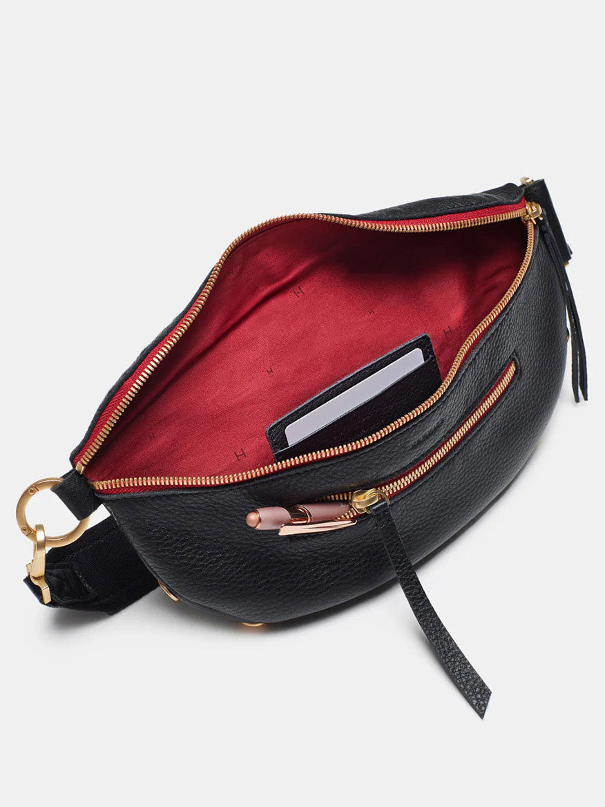 The Hammitt Los Angeles Charles Crossbody Medium in Black/Brushed Gold/Red Zip boasts a pebbled black leather exterior and a chic red interior. It opens to reveal compartments for pens, cards, and a front zipper pocket. Designed with a stylish strap and gold hardware accents, this versatile piece seamlessly transitions from crossbody bag to an elegant on-the-go companion.