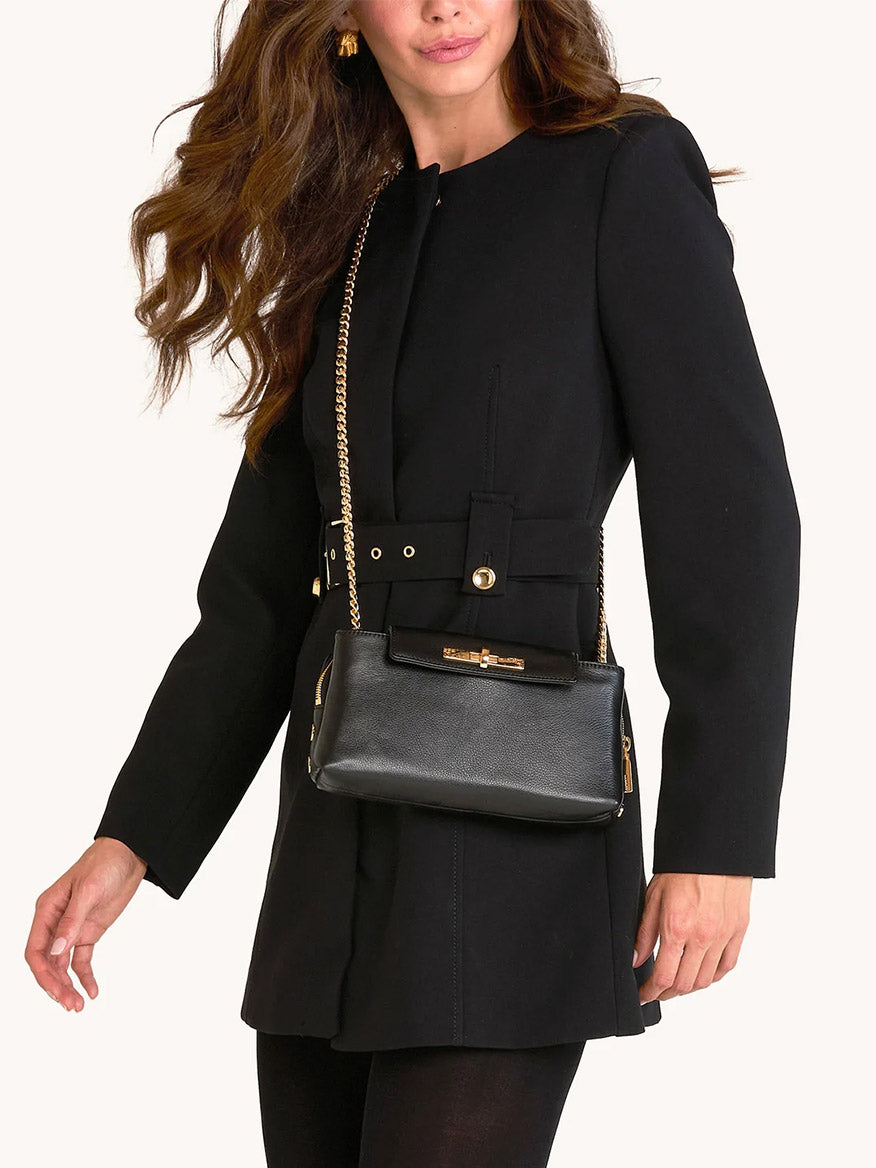 A woman wears a belted black coat and carries the Hammitt Los Angeles Charlotte Small crossbody bag in Black/Gold with a gold chain strap.