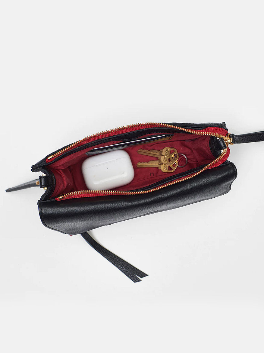 A small Hammitt Los Angeles Curtis in black & red zip wristlet unzipped to reveal contents including a red wallet, a brass keychain, and a white electronic device on a white background.