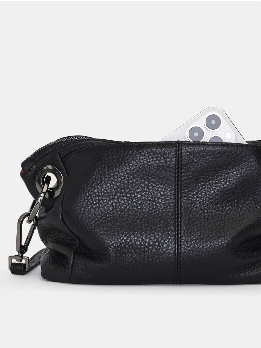 A Hammitt Los Angeles Daniel Crossbody Clutch Small in Black/Gunmetal, partially unzipped, reveals a smartphone with a triple-lens camera inside its black pebbled leather interior.
