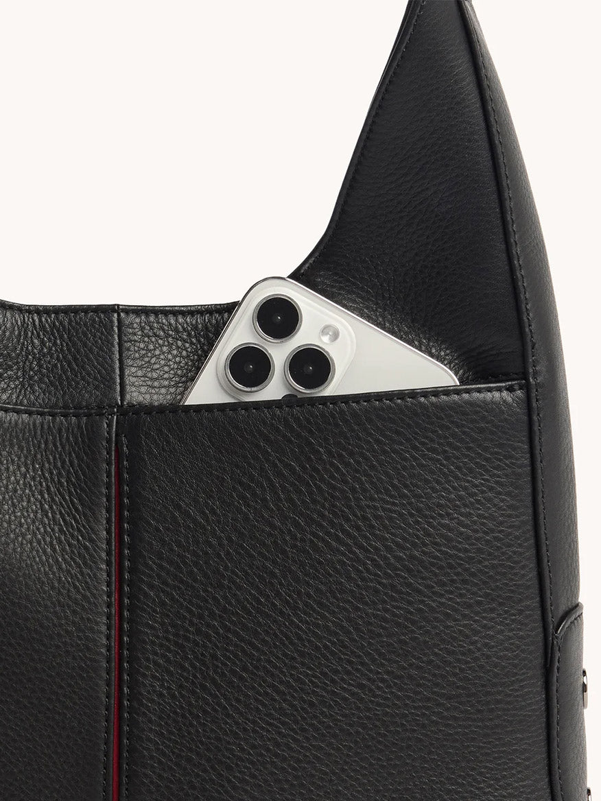 The Hammitt Los Angeles Tim Hobo in Black, crafted from pebbled leather with an exterior pocket and magnetic closure, securely holds a silver smartphone with three camera lenses.