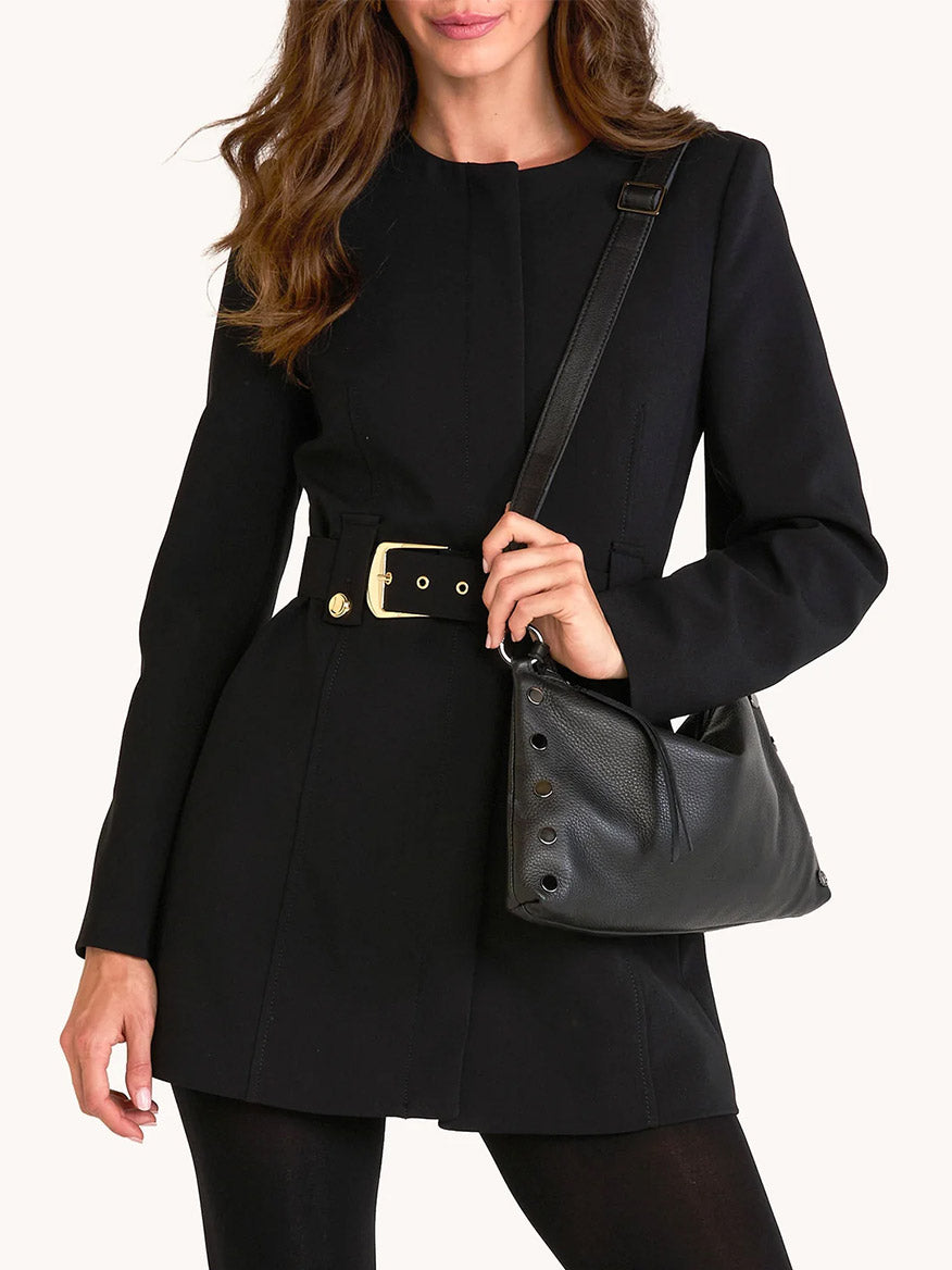 Woman wearing a black belted coat holds the Hammitt Los Angeles Kyle Medium Shoulder Bag in Black/Gunmetal, shown from shoulders to mid-thigh.