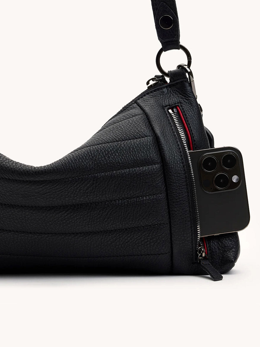The Hammitt Los Angeles Kyle Medium Shoulder Bag in Moto Black/Gunmetal features a textured finish and zippered pocket, shown partially unzipped to reveal a black smartphone—ideal for keeping essentials secure in style.