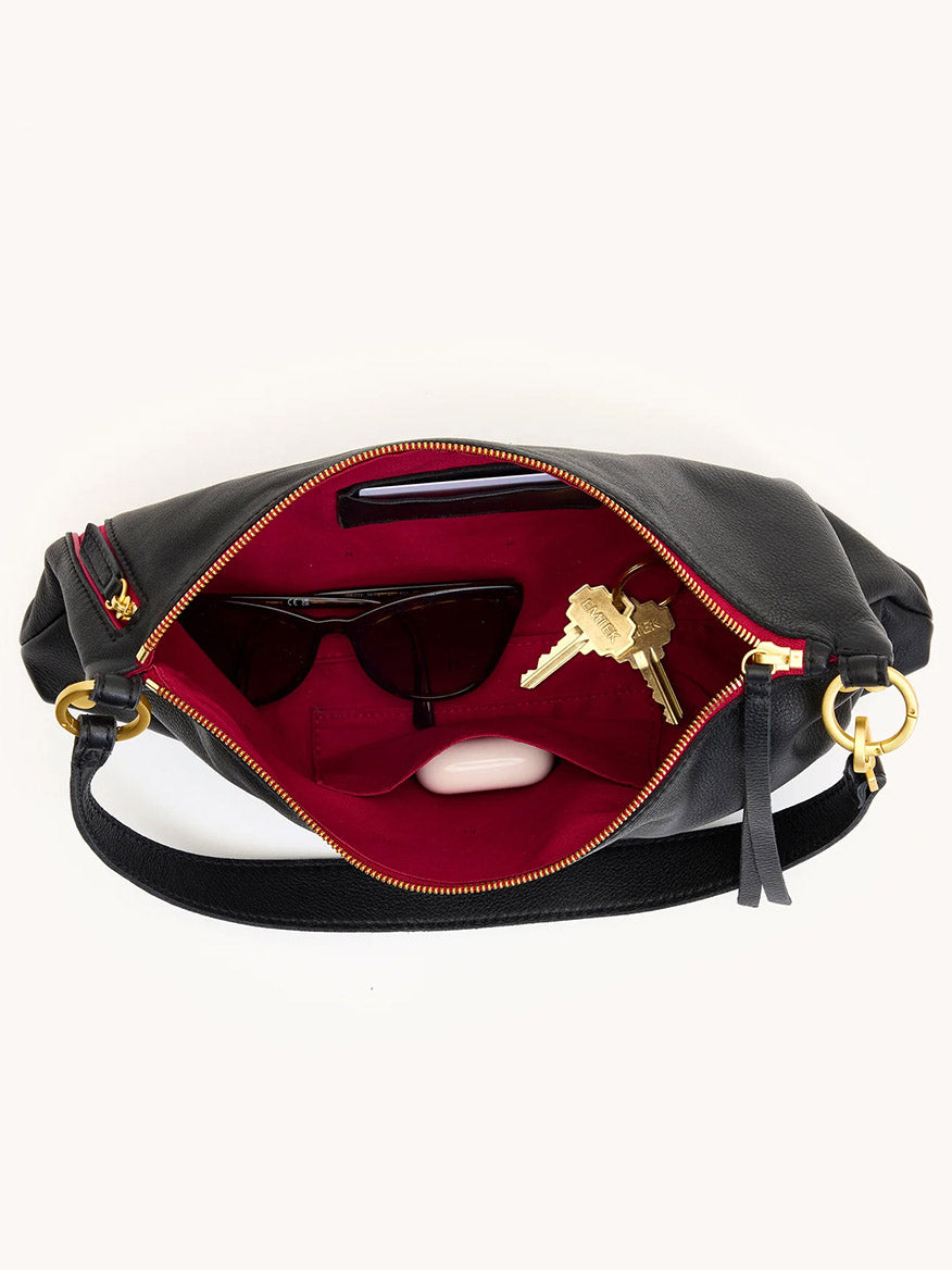 The Hammitt Los Angeles Kyle Medium Shoulder Bag in Black/Brushed Gold/Red Zip, shown from above with the zipper open, fits sunglasses, a phone, keys, and a small item—ideal for use as both a crossbody and shoulder bag.