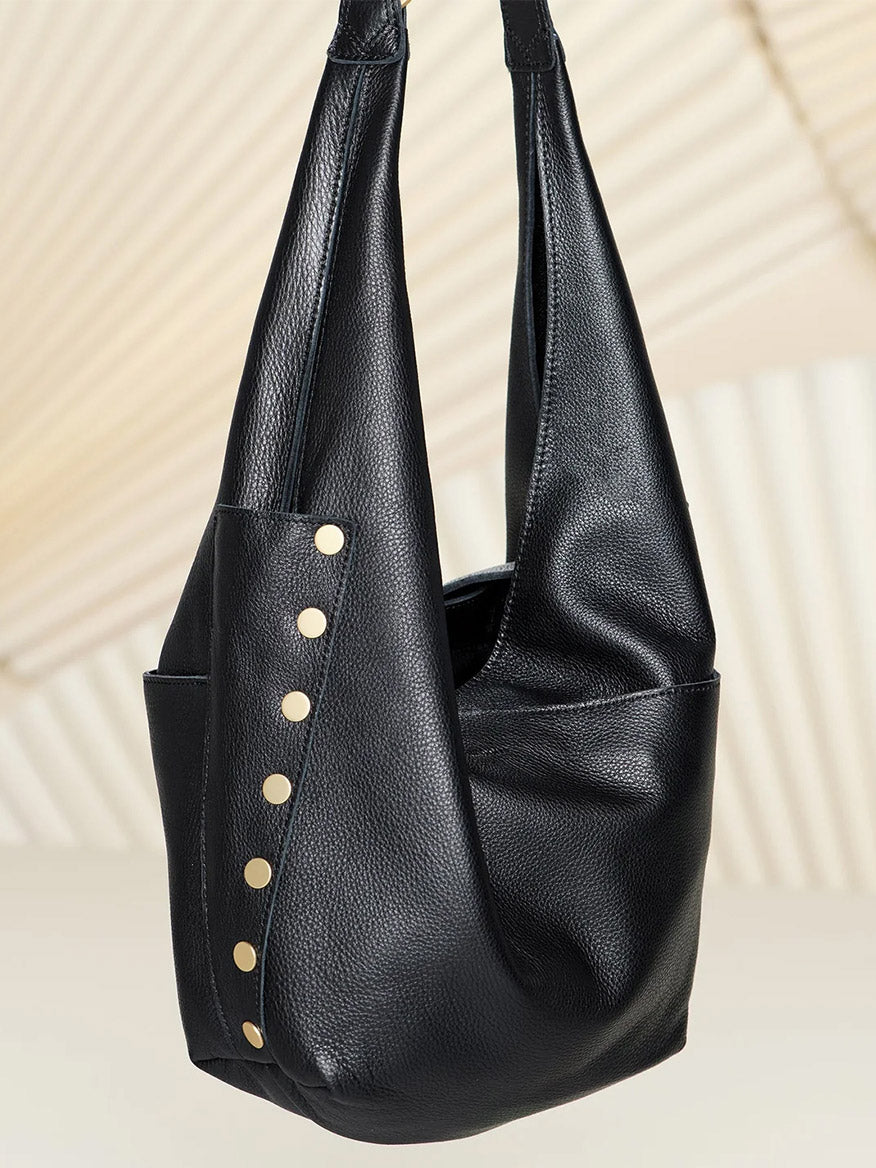 The Hammitt Los Angeles Tom Zip Large in Black/Brushed Gold/Red Zip is a spacious black leather hobo bag with gold studs, shown against a neutral backdrop—a stylish and roomy catch-all for your daily essentials.