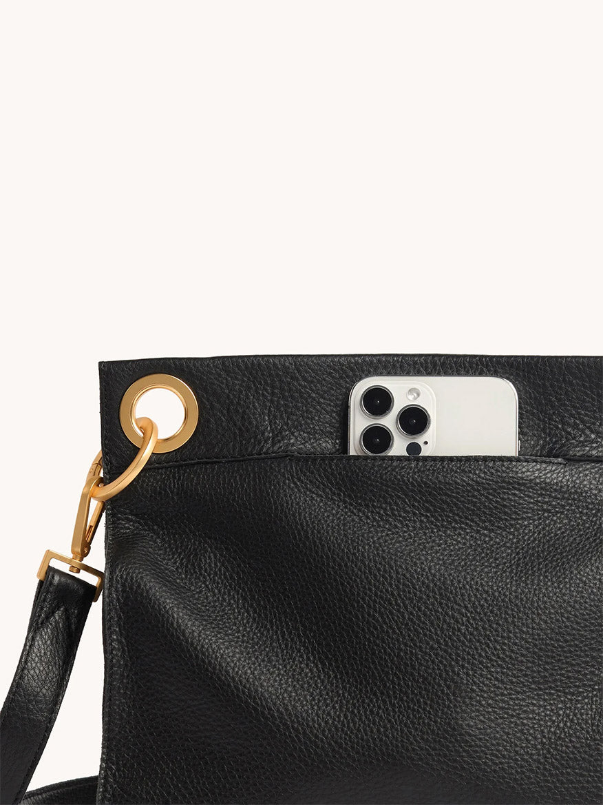The Hammitt Los Angeles Tony Large Crossbody Bag in North End is a black leather bag with a gold ring detail and adjustable strap, shown with an iPhone partially tucked into its exterior pocket against a plain background.