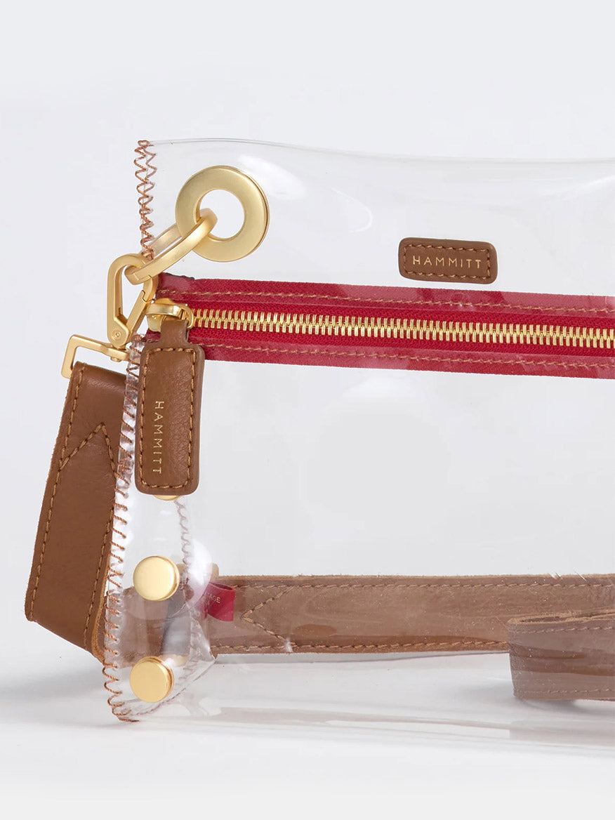 The Hammitt Los Angeles Tony Small Crossbody Bag features a clear, stadium-approved design with mahogany pebble leather trim, gold hardware, a red zipper, and the iconic Hammitt brand tag.