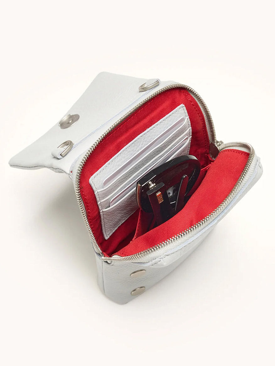 The Hammitt Los Angeles VIP Mobile in Bluebird/Brushed Silver is a compact crossbody in pastel blue pebbled leather with a white exterior and red interior, shown open to reveal card slots and sunglasses inside.