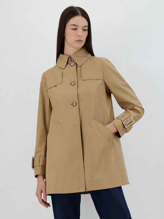 A woman modeling a Herno Delon and Monogram Trench Coat in Sabbia with button closures and buckle details, paired with dark jeans, standing against a plain white background.