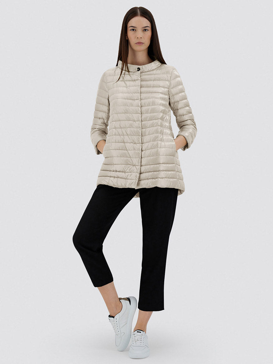 Woman wearing the Herno Rossella A-Shape Jacket in Chantilly, paired with black cropped pants and white sneakers, stands against a plain background with one leg crossed and hands in her pockets.