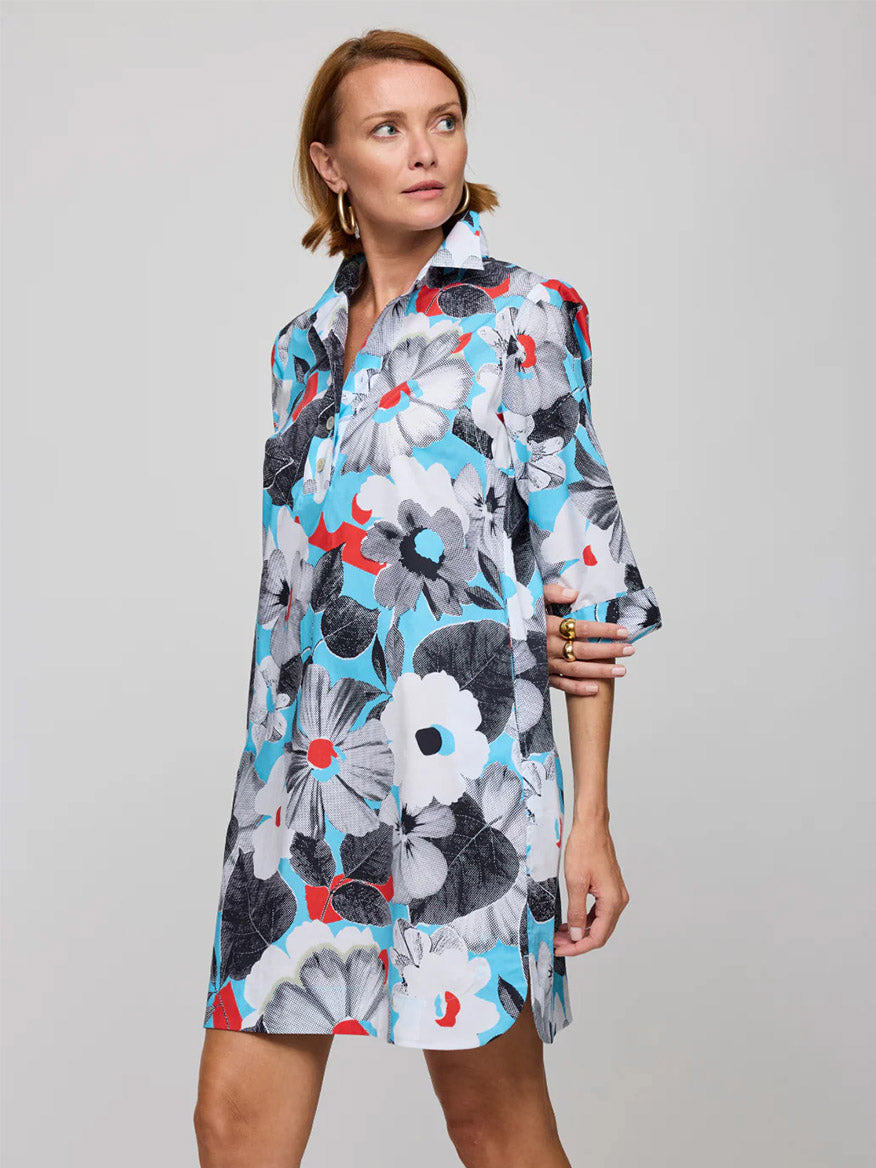 A woman wears the Hinson Wu Aileen 3/4 Sleeve Pop Art Flower Dress in Blue Combo, a loose-fitting shirtdress with bold, oversized floral prints in white, black, red, and blue on a gray background.