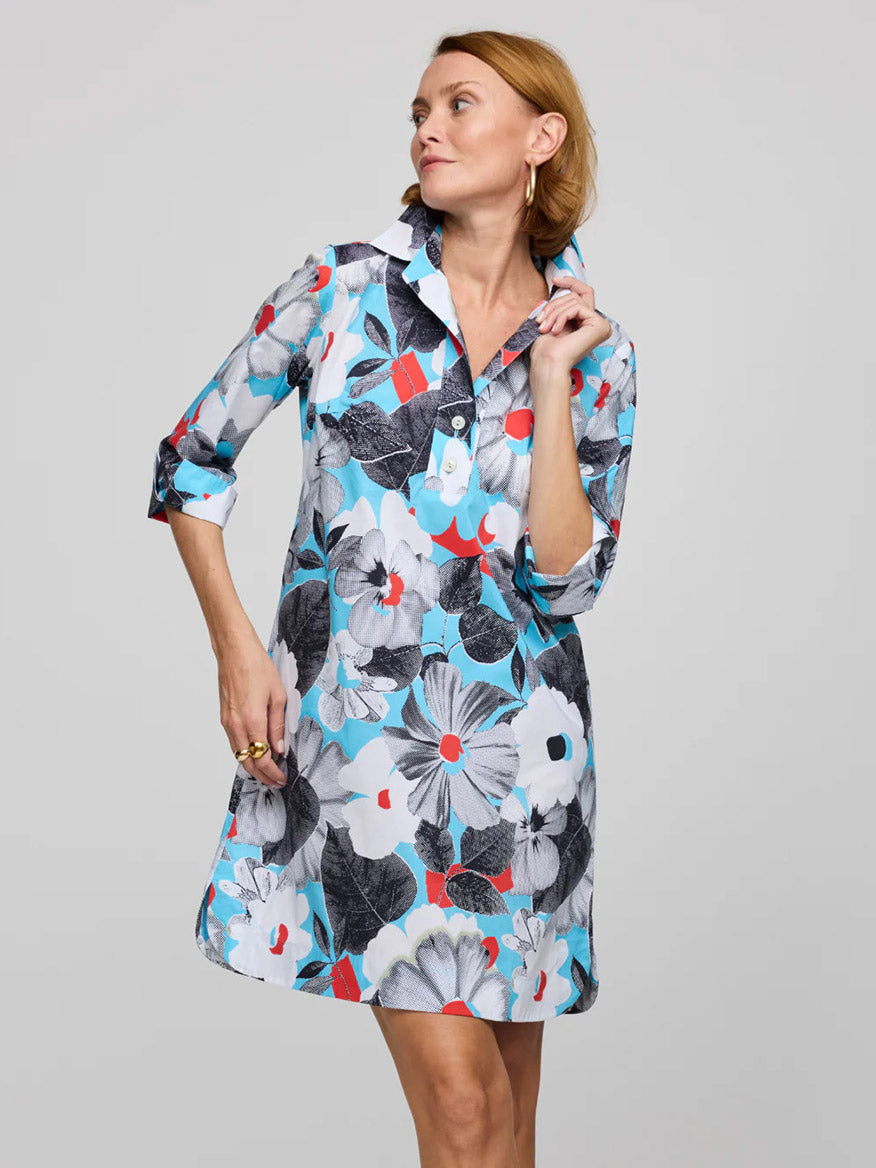 A woman wears the Hinson Wu Aileen 3/4 Sleeve Pop Art Flower Dress in Blue Combo, featuring bold black, white, red, and blue floral prints on refined cotton. She stands against a plain light gray background.
