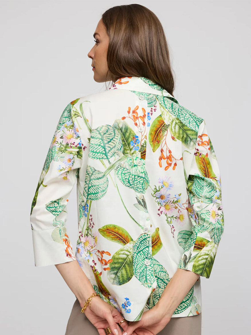 Against a plain backdrop, a person with long hair is seen from behind wearing the Hinson Wu Aileen 3/4 Sleeve Botanical Flora Print Shirt in Multi, featuring exclusive green and orange leaf prints. The refined cotton fabric gives the blouse a polished finish.