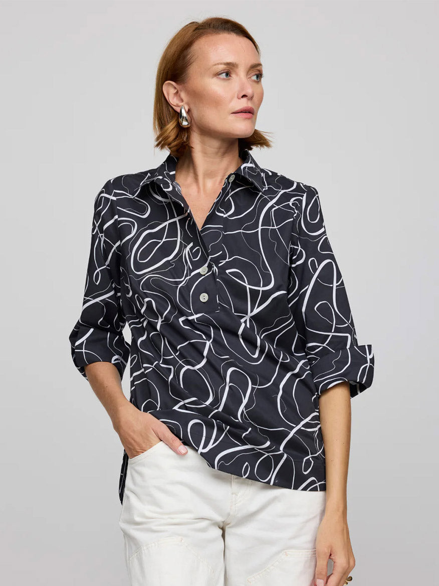 A woman wears the Hinson Wu Charlotte 3/4 Sleeve Ribbon Shirt in Black/White, featuring exclusive white abstract line prints, paired with white pants, crafted from a refined cotton blend, standing against a plain gray background.
