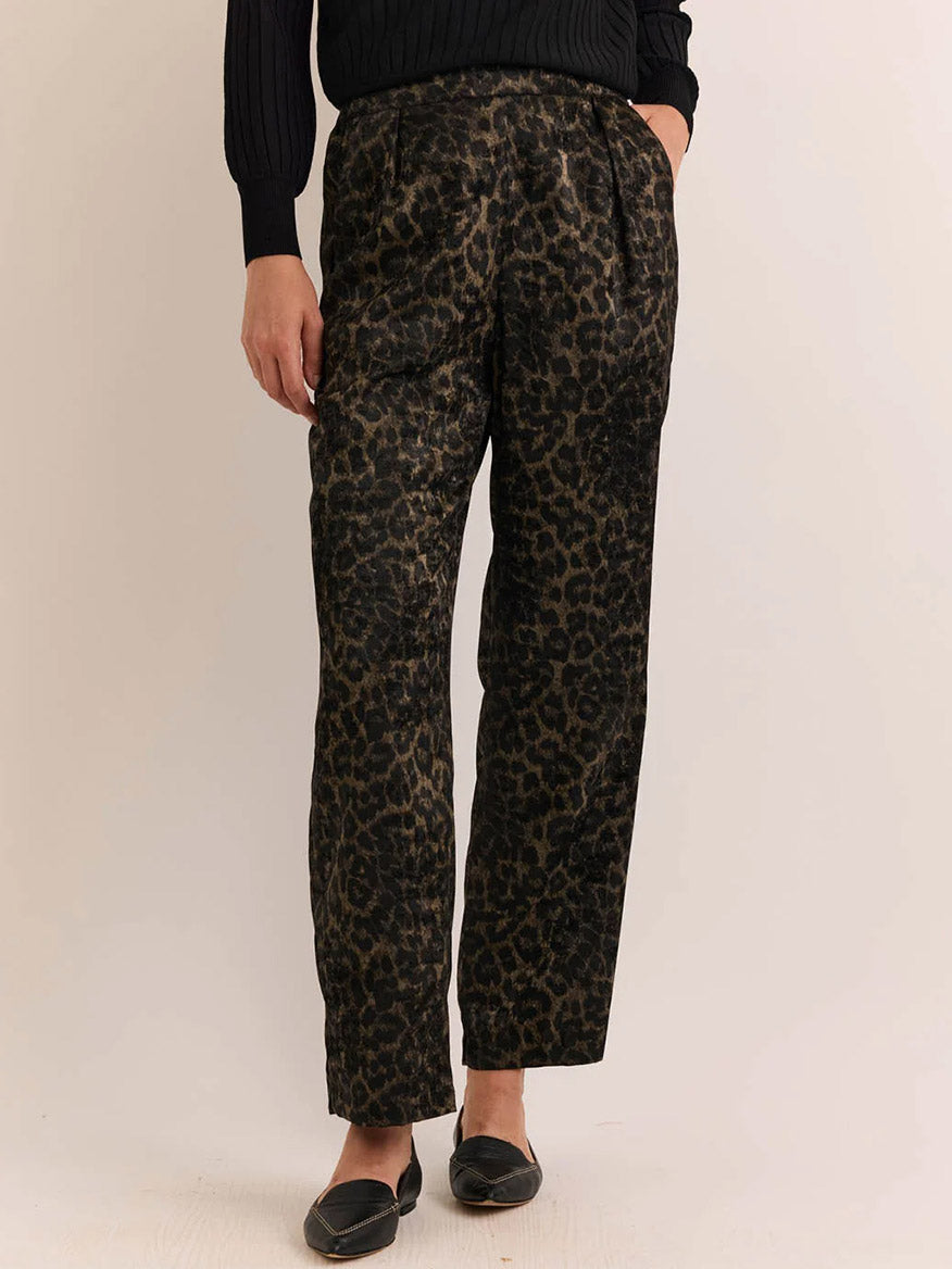 Wearing the Hinson Wu Hostess Animal Print Pant in Animal Print—relaxed straight leg black and brown leopard print pants crafted from foil print fabric—paired with a black long-sleeve sweater and black flats, this person stands against a plain background.