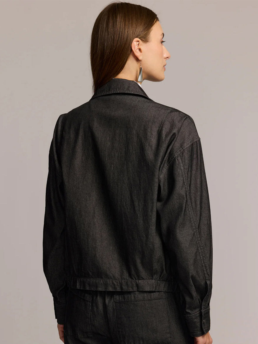 A woman faces away, wearing the Hinson Wu Louise Long Sleeve Denim Jacket in Black Wash with matching pants against a plain background.