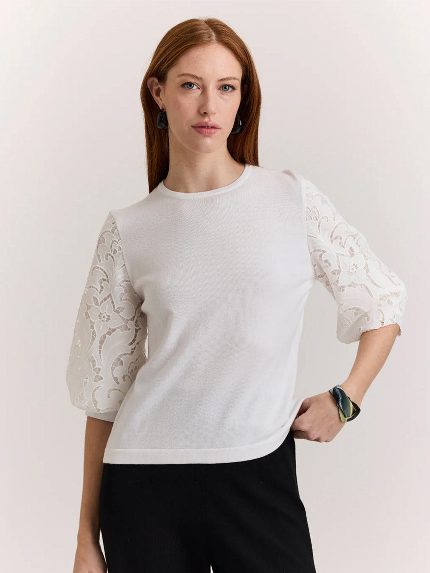 A woman with long auburn hair wears the Hinson Wu Millie Lace Elbow Sleeve Sweater in white and black pants, standing with one hand on her hip against a plain background.