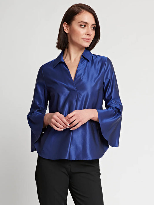 Woman standing with hands lightly clasped, wearing a Hinson Wu Nicole Bracelet Sleeve Silk Satin Top in Royal and black trousers, against a neutral background.