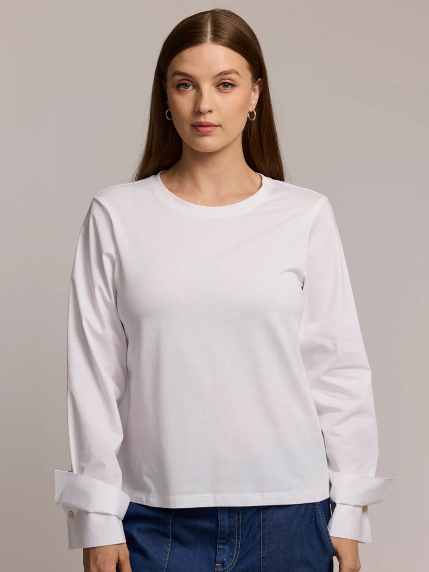 A woman with long brown hair models the Hinson Wu Reagen Long Sleeve Foundation Layer in White with blue jeans, standing against a neutral background.