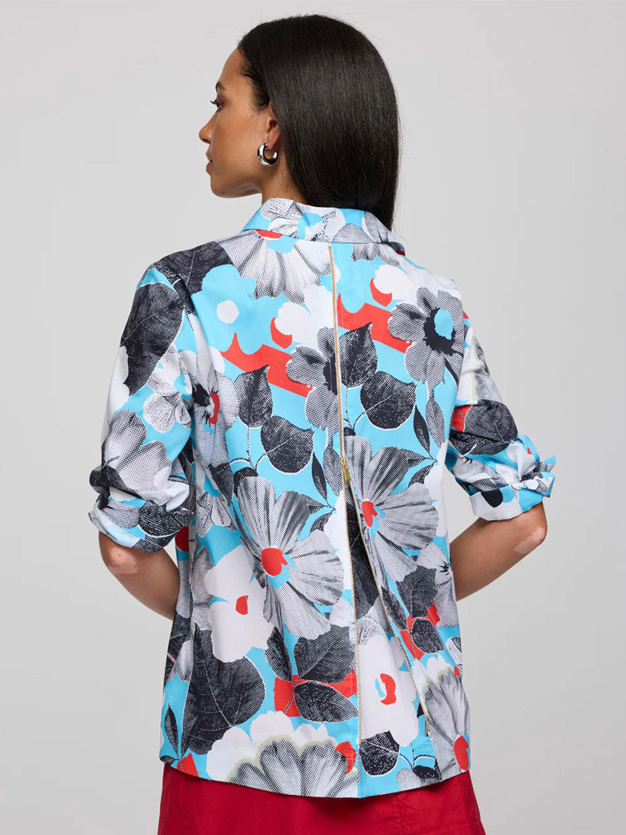 A woman with long dark hair faces away, wearing the Hinson Wu Xena 3/4 Sleeve Pop Art Flower Shirt—a refined cotton piece featuring exclusive bold blue, black, white, and red floral prints; her sleeves are rolled up.