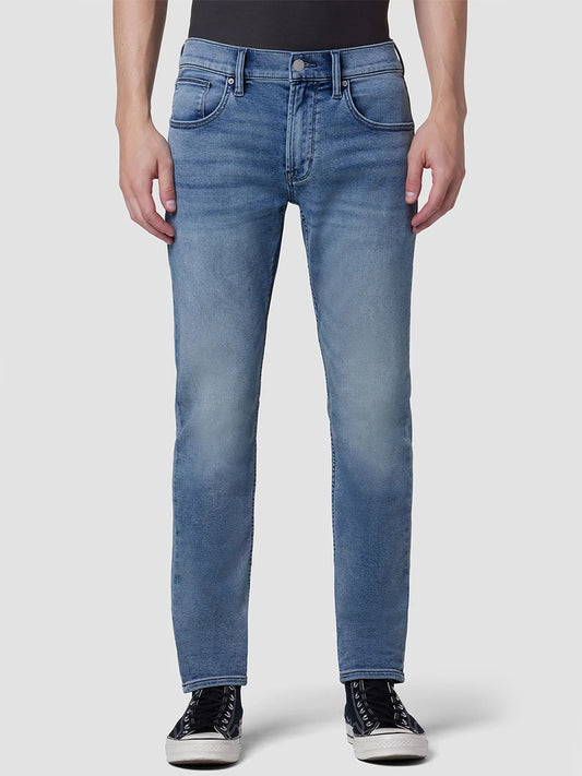 Person wearing Hudson Blake Slim Straight Jeans in Palisades and black sneakers standing with hands at sides.