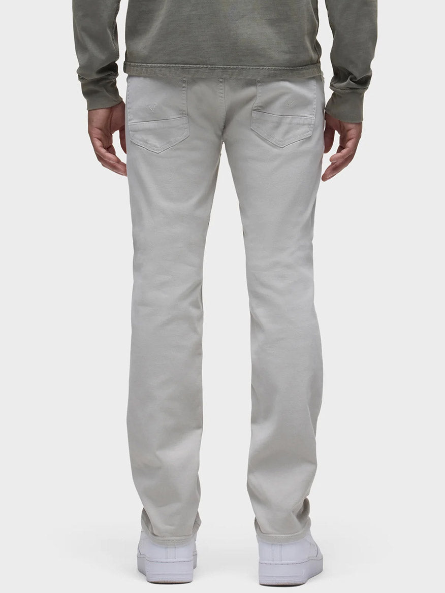 A person wearing a green long-sleeve shirt and Hudson Blake Slim Straight Twill Pant in Ash stands facing away, with classic five-pocket detailing subtly visible and white shoes against a plain background.